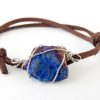 close up of iridescent blue titanium stone wrapped in cabled Stainless Steel on adjustable brown suede bracelet