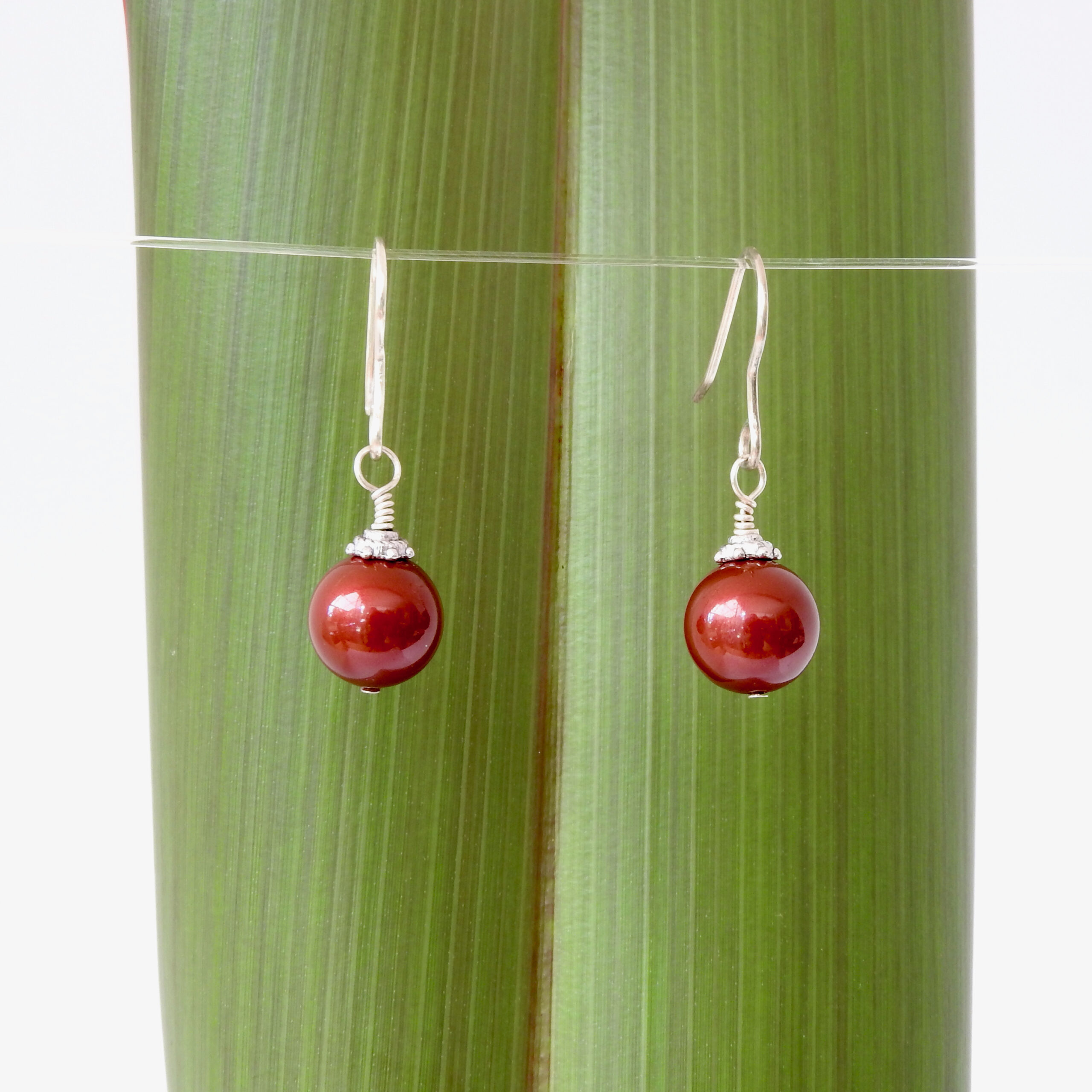 Burgundy Swarovski Pearl Christmas bauble earrings against flax
