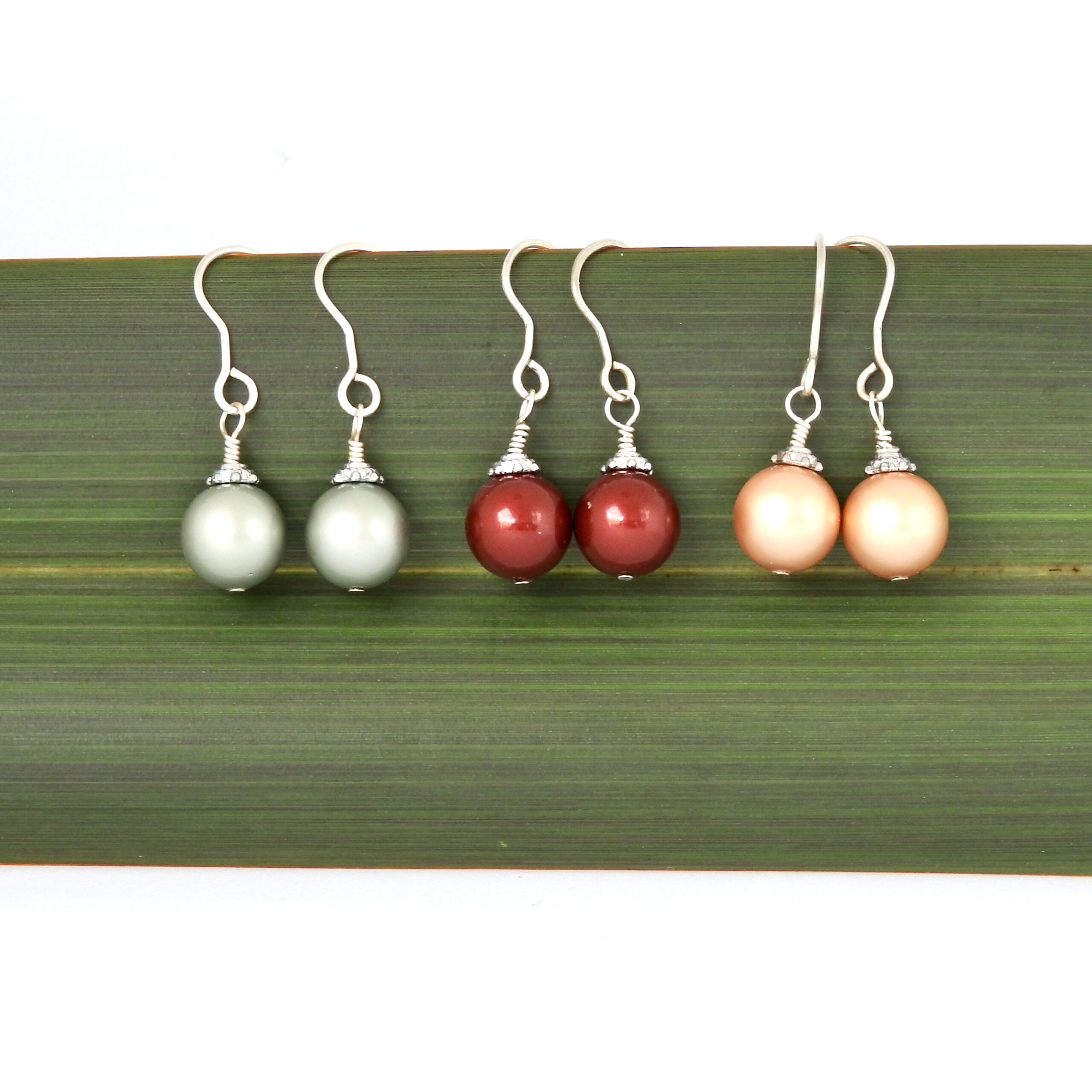 Christmas Bauble Earrings in Green, Burgundy and Gold hanging against flax backdrop