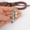 Turquoise and peach coloured bag charm or key ring shown with a hand for scale