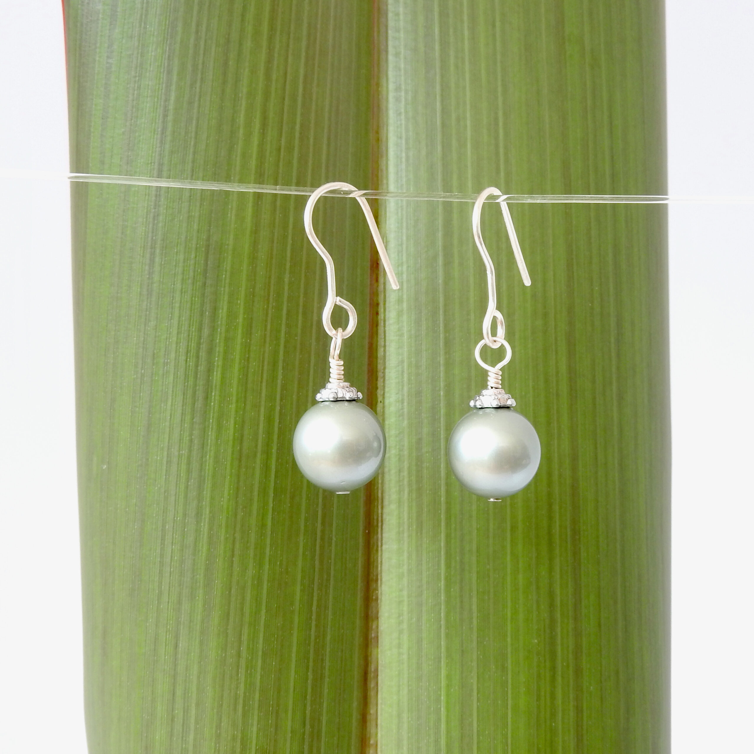 Pale Green Swarovksi Pearl Christmas Bauble Earrings shown against flax
