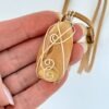 Hand showing Kauri Gum necklace with Caramel suede adjustable cord on white background