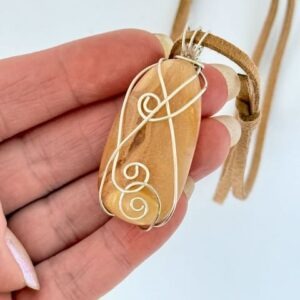 Hand showing Kauri Gum necklace with Caramel suede adjustable cord on white background