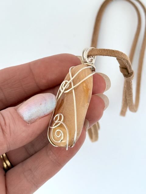 Hand showing front side of Kauri Gum neckalce_white background