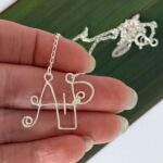 Custom Sterling Silver A+P Initial Letter Necklace showing hand scale against flax background